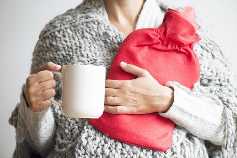 Lady holding a hot tea and hot water bottle rugged up